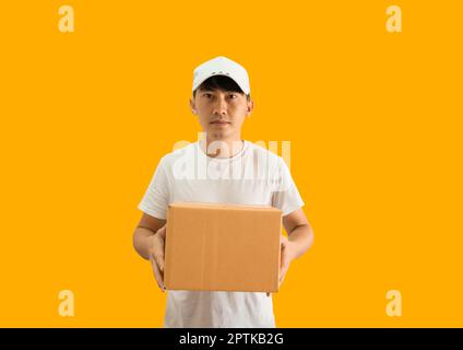 Jeune homme de livraison asiatique portant une casquette et un t-shirt blanc vierge tenant une boîte postale isolée sur fond jaune. concept de service de livraison express. Banque D'Images