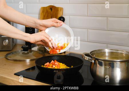 Vue rapprochée de la main femelle met des légumes hachés dans une poêle. Processus de préparation de la sauce végétale. Banque D'Images