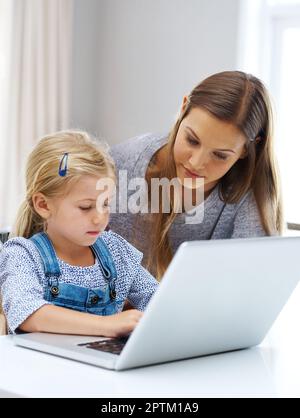 Shes sérieux au sujet de l'amélioration de ses compétences INFORMATIQUES. une jeune mère aidant sa petite fille avec l'ordinateur portable Banque D'Images