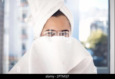 Portrait, serviette et femme après une douche, heureux et se détendre tout en cachant le visage et le toilettage dans sa maison. Timide, fille et beauté, soin de la peau et routine en ba Banque D'Images