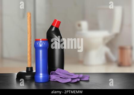 Différentes fournitures de nettoyage de toilettes sur table noire dans la salle de bains, espace pour le texte Banque D'Images