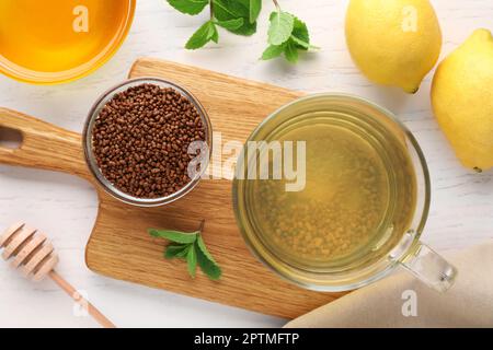 Tasse de thé de sarrasin aromatique, granulés, citrons, menthe et miel sur table en bois blanc, plat Banque D'Images