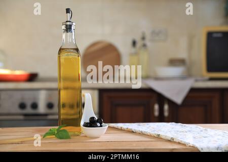 Bouteille d'huile de cuisson, olives et basilic sur table en bois dans la cuisine, espace pour le texte Banque D'Images