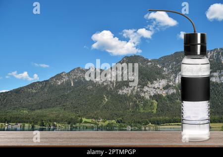 Bouteille de sport avec eau douce sur table en bois et belle vue sur les montagnes, espace pour le texte Banque D'Images