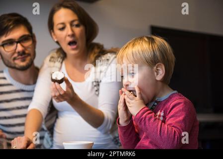 Petit garçon mangeant le dessert avec la bouche ouverte tandis que les parents sont choqués, Munich, Allemagne Banque D'Images
