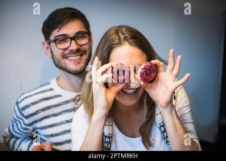 Femme regardant à travers des donuts pendant que mari montres, Munich, Allemagne Banque D'Images