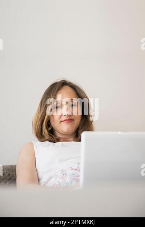 Femme enceinte assise sur un canapé et travaillant sur un ordinateur portable, Munich, Bavière, Allemagne Banque D'Images