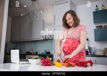 Femme enceinte coupant des légumes frais dans la cuisine, Munich, Bavière, Allemagne Banque D'Images