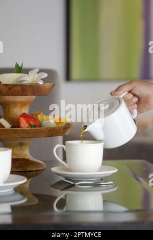 Femme main tenant une théière et versant du thé dans une tasse en céramique blanche Banque D'Images