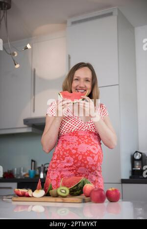 Portrait d'une femme enceinte qui mange de la pastèque dans la cuisine, Munich, Bavière, Allemagne Banque D'Images