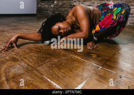 La danseuse contemporaine noire se déplace sur le sol avec une jupe colorée Banque D'Images