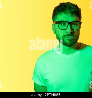 Portrait créatif d'un homme d'âge moyen barbu avec des lunettes noires encadrées. Un homme déprimé avec des problèmes mentaux regarde malheureusement loin. Lumière verte colorée Banque D'Images