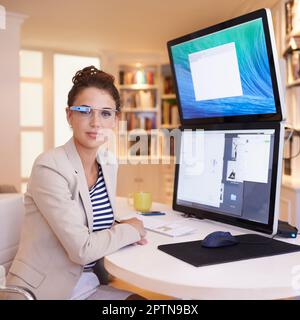 Ses a trouvé un mode de travail plus intelligent. Portrait d'une jeune femme portant des lunettes intelligentes tout en travaillant sur un ordinateur à deux écrans Banque D'Images