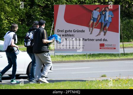 Une grande affiche appelant aux élections sociales de 2023 sur 31 mai 2023 se trouve dans une rue très fréquentée, trois jeunes marchent devant elle. Elle a lieu tous les six ans pour tous les prestataires d'assurance-retraite, d'assurance-maladie et d'assurance-accident. Oberhausen, 27 avril 2023 Banque D'Images