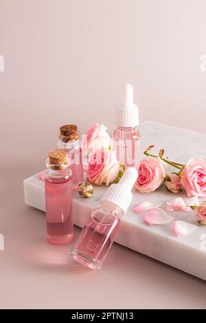 Un ensemble de cosmétiques et d'eau de rose en bouteilles de verre parmi de petites roses fraîches sur un podium en marbre blanc. Vue verticale Banque D'Images