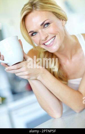Elle apprécie une bonne tasse de café. Belle jeune femme blonde appréciant une délicieuse tasse de café fraîchement préparée. Banque D'Images