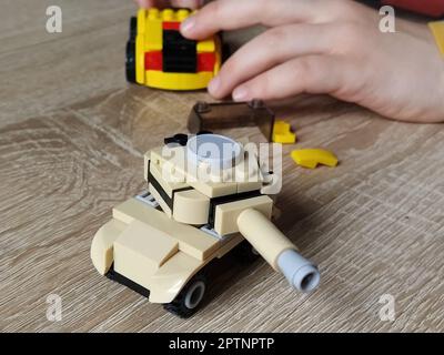 Char à jouets sur une table en bois. Jouet en plastique. Artisanat d'un concepteur pour enfants. La couleur beige du réservoir, une image défocuée autour des bords. Main des enfants Banque D'Images