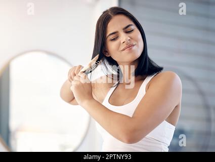 Cheveux, brosse et extrémités fractionnées avec une femme dans la salle de bains de sa maison, se brossant ses nœuds pour le toilettage. Stress, beauté et soin des cheveux avec un yo frustré Banque D'Images