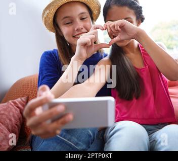 Faisons un selfie de coeur. deux amis adolescents prenant un selfie tout en faisant une forme de coeur avec leurs mains. Banque D'Images
