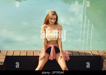 Magnifique jeune femme calme est assise sur un parquet dans la piscine publique Banque D'Images