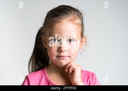 Gros plan pensif, joli blond petit enfant, fille avec blessure, rayure avec de l'iode sur le visage sur fond blanc. Maltraitance d'enfants, blessures physiques. Social i Banque D'Images