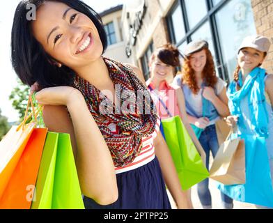 Elle a cette lueur d'après-boutique. Une belle fille ethnique tenant des sacs de shopping et souriant avec ses amis en arrière-plan Banque D'Images