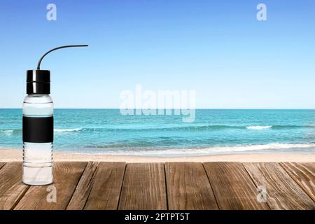 Bouteille de sport avec eau douce sur une table en bois et belle vue sur la plage de sable près de la mer, espace pour le texte Banque D'Images