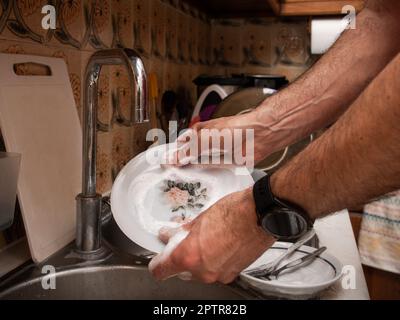 Les hommes lavent la vaisselle avec de la mousse détergente dans un ancien évier de cuisine tout en maintenant le robinet fermé. Économiser de l'eau sur les tâches ménagères Banque D'Images