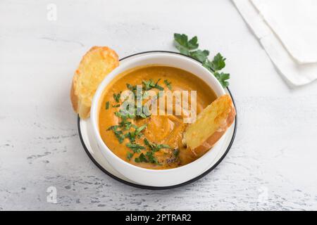 Soupe à la crème végétalienne de lentilles rouges et de légumes avec du lait de coco arrosé de persil haché dans un bol blanc et de croûtons de fromage sur un b gris clair Banque D'Images