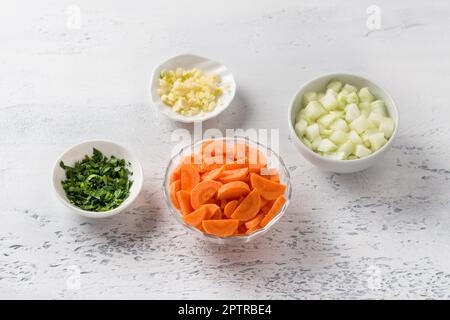 Bols avec carottes, oignons, ail et persil haché sur fond gris clair, vue du dessus. Cuisine délicieux ragoût végétarien maison Banque D'Images