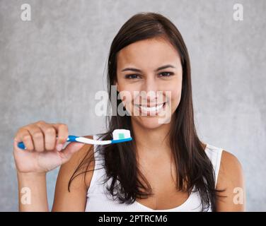 An isolated portrait of a young woman happily brushing her teeth. Stock Photo