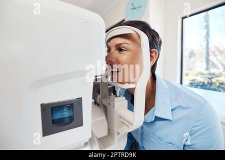 Un test oculaire, un examen ou un dépistage de la vision et de la vue chez l'optométriste ou l'opticienne avec une jeune femme. Tester sa vue avec un réfracto automatique Banque D'Images