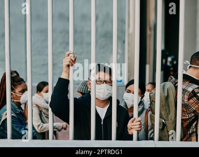 Derrière les barreaux, le verrouillage et les restrictions de covid avec un homme portant un masque pendant une pandémie et l'interdiction de voyager. Portrait d'un homme enfermé pendant le TH Banque D'Images