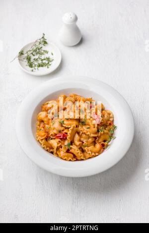 Pâtes simples à la sauce tomate saupoudrées de thym frais dans une assiette blanche sur fond gris clair, vue de dessus, plat. Délicieux plats faits maison Banque D'Images