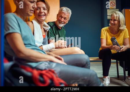 Groupe de poeple sportif dans le dressing de la salle de gym, assis et ayant la conversation. Homme âgé et femmes avec une jeune femme ensemble. Banque D'Images