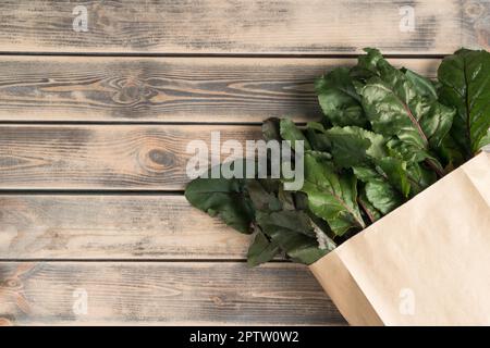 Feuillage vert luxuriant et tiges de racines de betteraves se cachant dans un sac écologique, emballage sur fond de bois. Achats écologiques, livraison de nourriture et légumes de ferme bio Banque D'Images