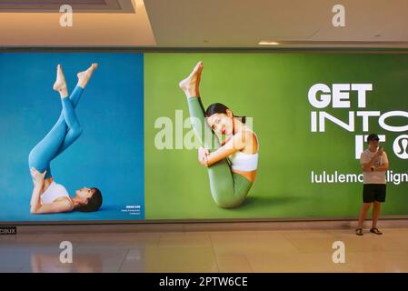 À ION Orchard (centre commercial), Orchard Road, Singapour, un jeune homme se tient devant les publicités sur le thème du yoga pour co. « Lulululemon » qui vend des vêtements de sport Banque D'Images