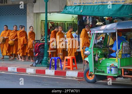 Des moines bouddhistes débutants qui descendent dans une rue dans un dossier ordonné pour recevoir des almes, passant un tuk-tuk sur leur chemin ; Bangkok, Thaïlande Banque D'Images