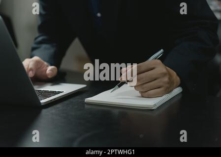 Homme d'affaires main tenant stylo écriture sur ordinateur portable travail avec ordinateur portable dans le bureau moderne.écrire sur le concept journal intime. Banque D'Images