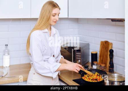 Une femme mignonne mélange des légumes dans une poêle à frire Banque D'Images