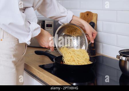 La vue rapprochée des mains des femmes met des spaghetti sur une poêle. Banque D'Images