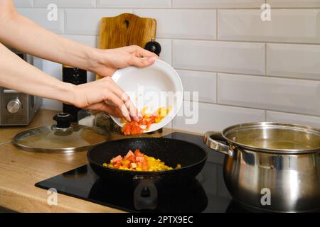 Vue rapprochée de la main femelle met des légumes hachés dans une poêle. Processus de préparation de la sauce végétale. Banque D'Images