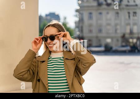Une femme souriante met des lunettes de soleil à l'extérieur de la ville Banque D'Images