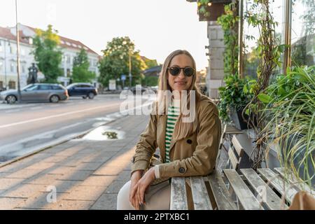 Une femme en lunettes de soleil se trouve à la table d'un café extérieur Banque D'Images