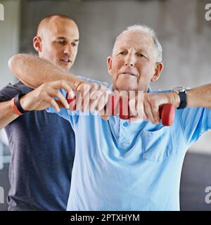 Vivez longtemps et favorisez des habitudes de remise en forme saines. un homme âgé qui travaille avec l'aide d'un formateur Banque D'Images