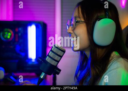Asiatique jeune gamer femme porter des écouteurs jouer à des jeux vidéo en ligne sur ordinateur elle en direct et de discuter avec des fans, heureux streamer femme parlant avec Banque D'Images