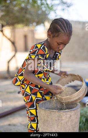 Une fillette tamise le grain de mil tout en l'estampant dans la farine dans la région de Ségou, au Mali, en Afrique de l'Ouest. 2022 Mali sécheresse et crise de la faim. Banque D'Images