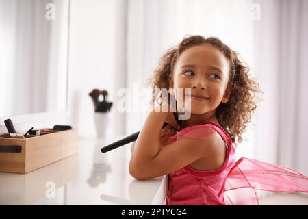 Apprendre les tenants et les aboutissants de la beauté dès le plus jeune âge. une petite fille jouant avec le maquillage devant le miroir Banque D'Images