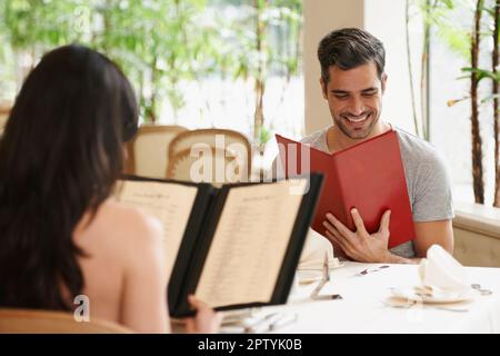 Tout a l'air délicieux. Un jeune couple heureux regardant leurs menus dans un restaurant chic Banque D'Images