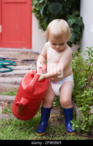 Curieux de savoir comment fonctionne la nature. Un adorable petit garçon qui abreuve le jardin Banque D'Images